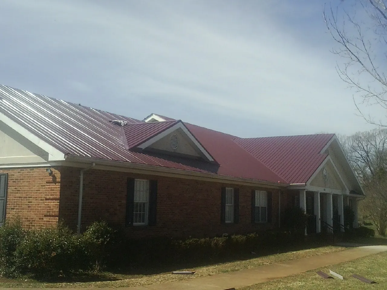 Red metal roof with gabled entries on a long brick building, from a Hail Damage Roof Repair job in Herman