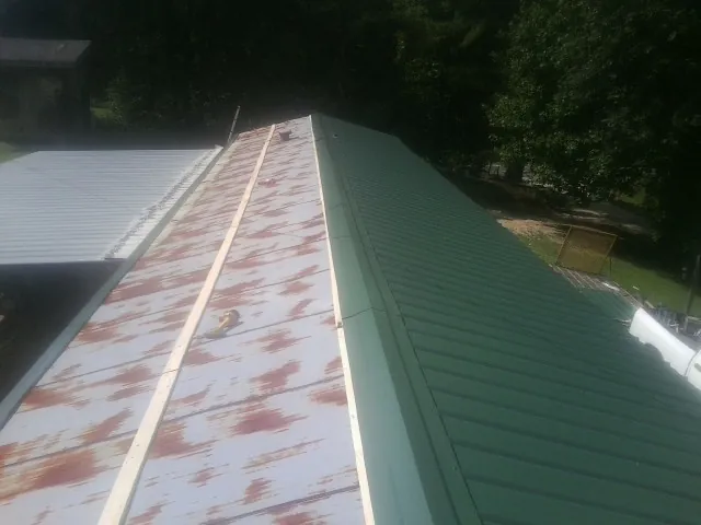 Old rusted panels beside newly installed green metal roofing — Wind Damage Roof Repair by Roofing Brothers in Herman