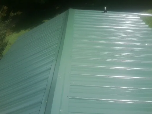 New green metal panels meeting at the ridge of a roof — Flat Roof Repair work by our crew in Herman