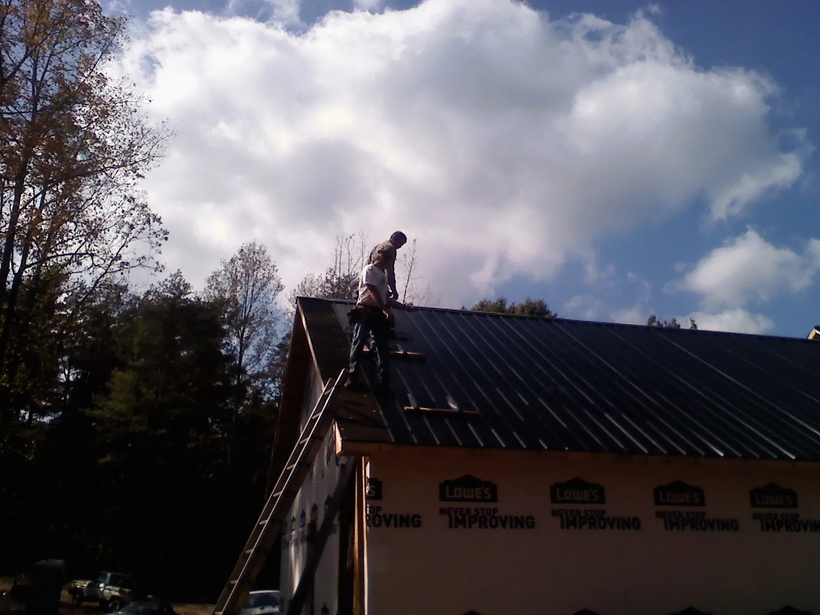 Roofer fastening dark metal panels high against a cloudy sky, from a Roof Inspection job in Herman