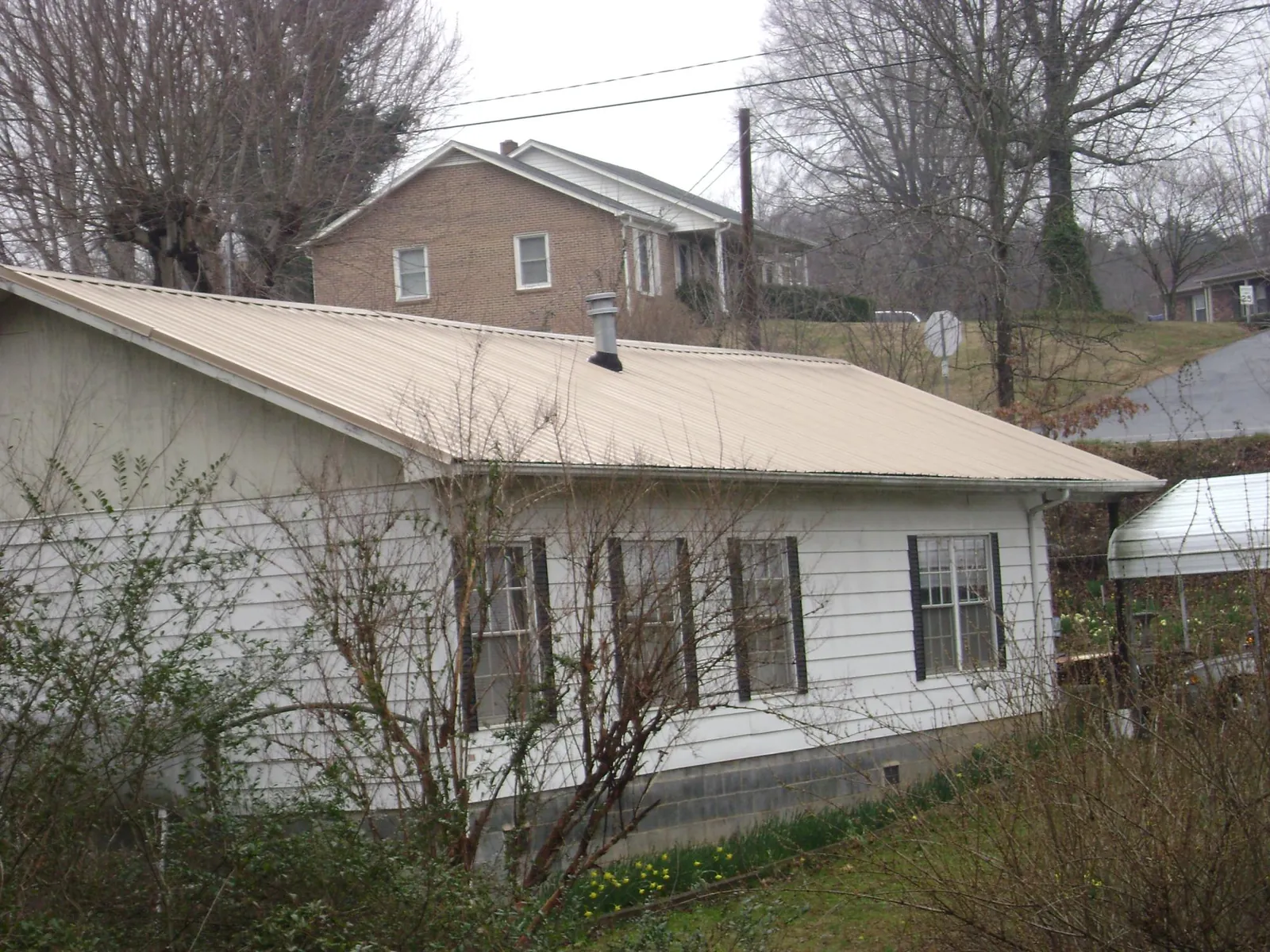 Tan metal roof on a white sided house set into a hillside — Commercial Roofing by Roofing Brothers in Herman