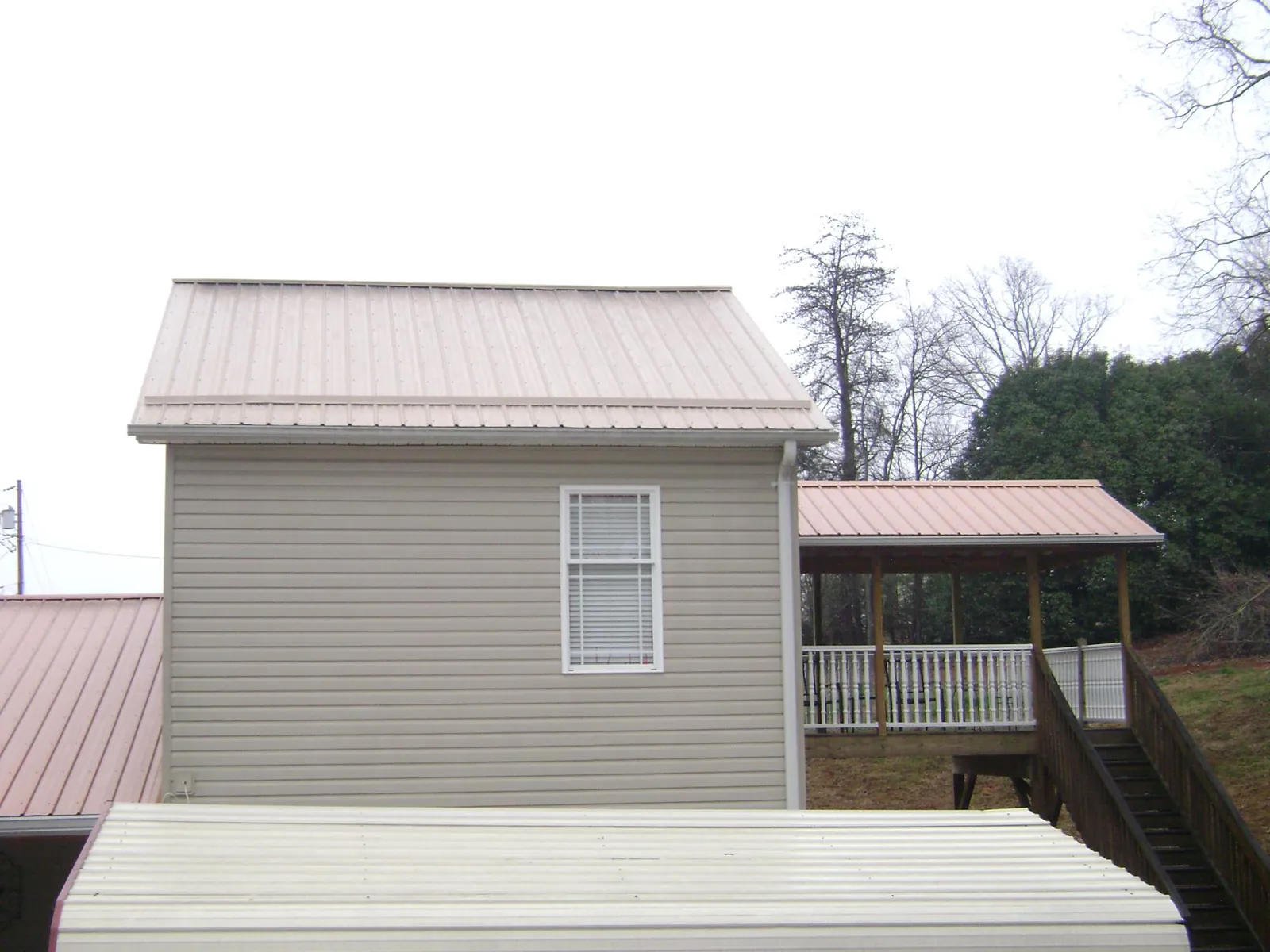 Tan metal roofs on a two story addition and attached porch, from a Roof Replacement job in Herman